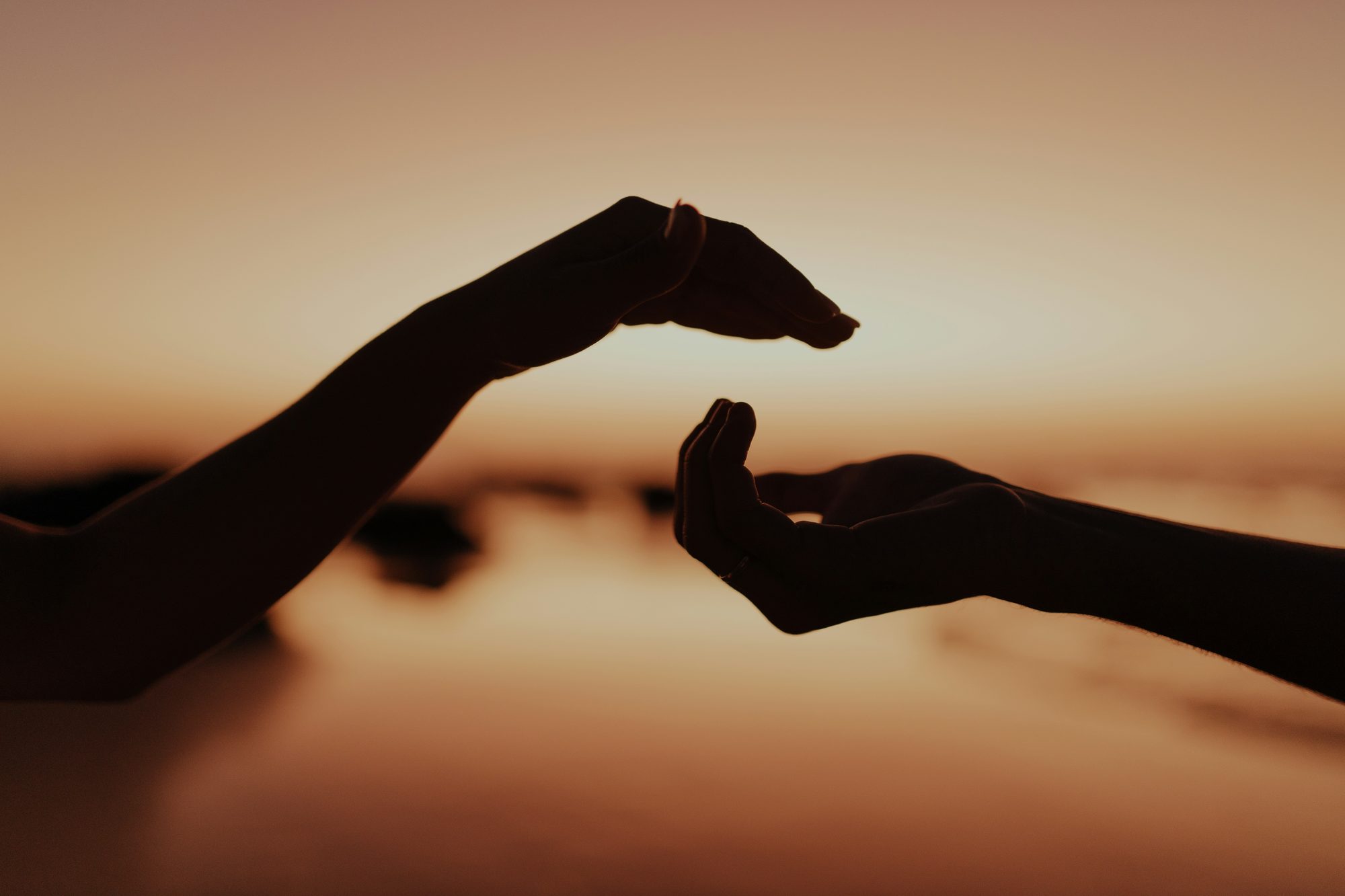 Two hands reaching toward each other at golden sunset